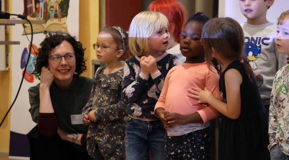 Erzieherin kniet neben einer Gruppe fröhlicher Kindergartenkinder bei einer Auszeichnungsveranstaltung.