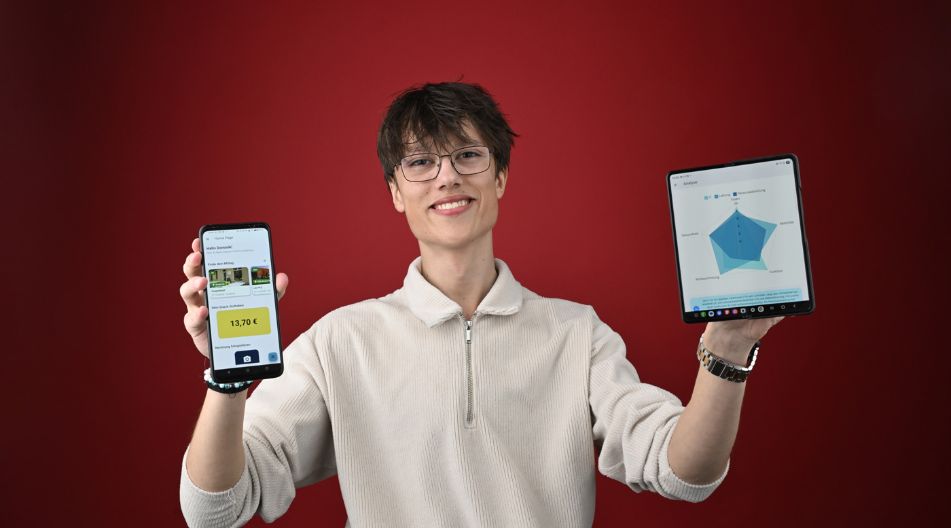 Ein junger Erwachsener hält vor einer roten Wand ein Smartphone und ein Tablet in die Kamera. Darauf ist seine eigens entwicktelte App zu sehen.